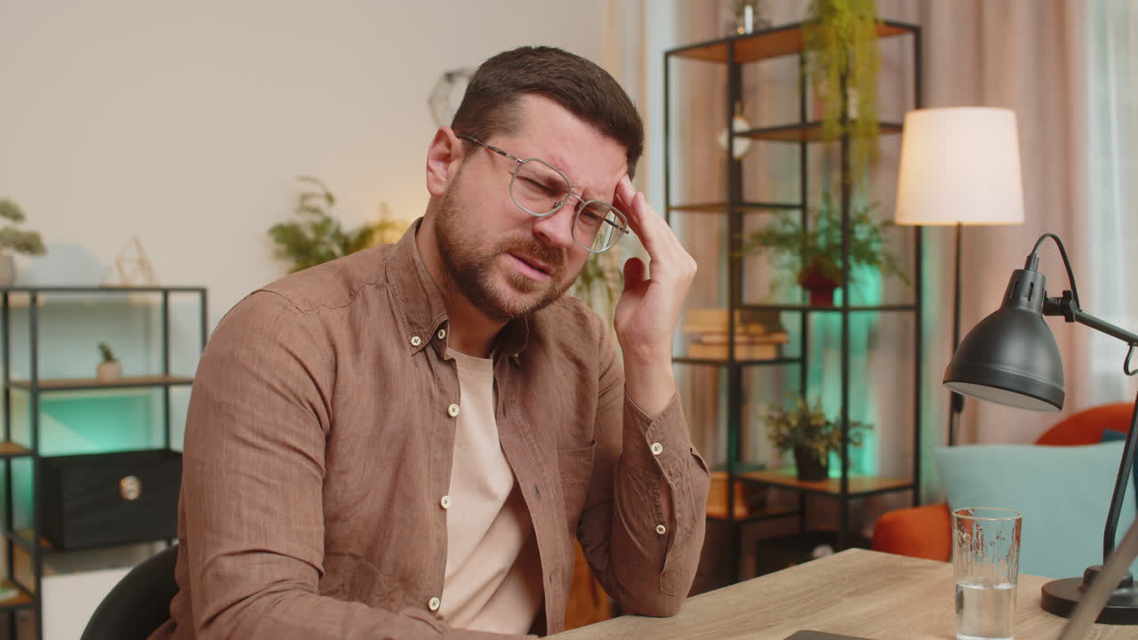 Tired ill caucasian man using laptop and suffering from headache problem tension sitting at table