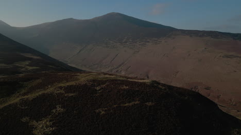 Hiker-walking-on-mountain-with-orbit-reveal-of-misty-mountains-and-green-valley-with-natural-lens-flare-in-English-Lake-District-UK