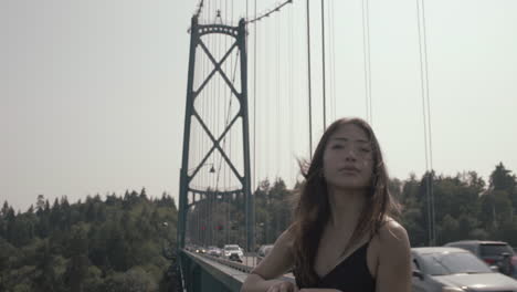 wide tilt down shot of asian woman enjoying beautiful view from lions gate bridge, traffic and park in background, slowmo