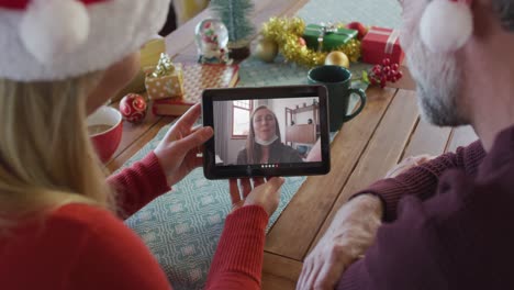 Caucasian-couple-with-santa-hats-using-tablet-for-christmas-video-call-with-woman-on-screen