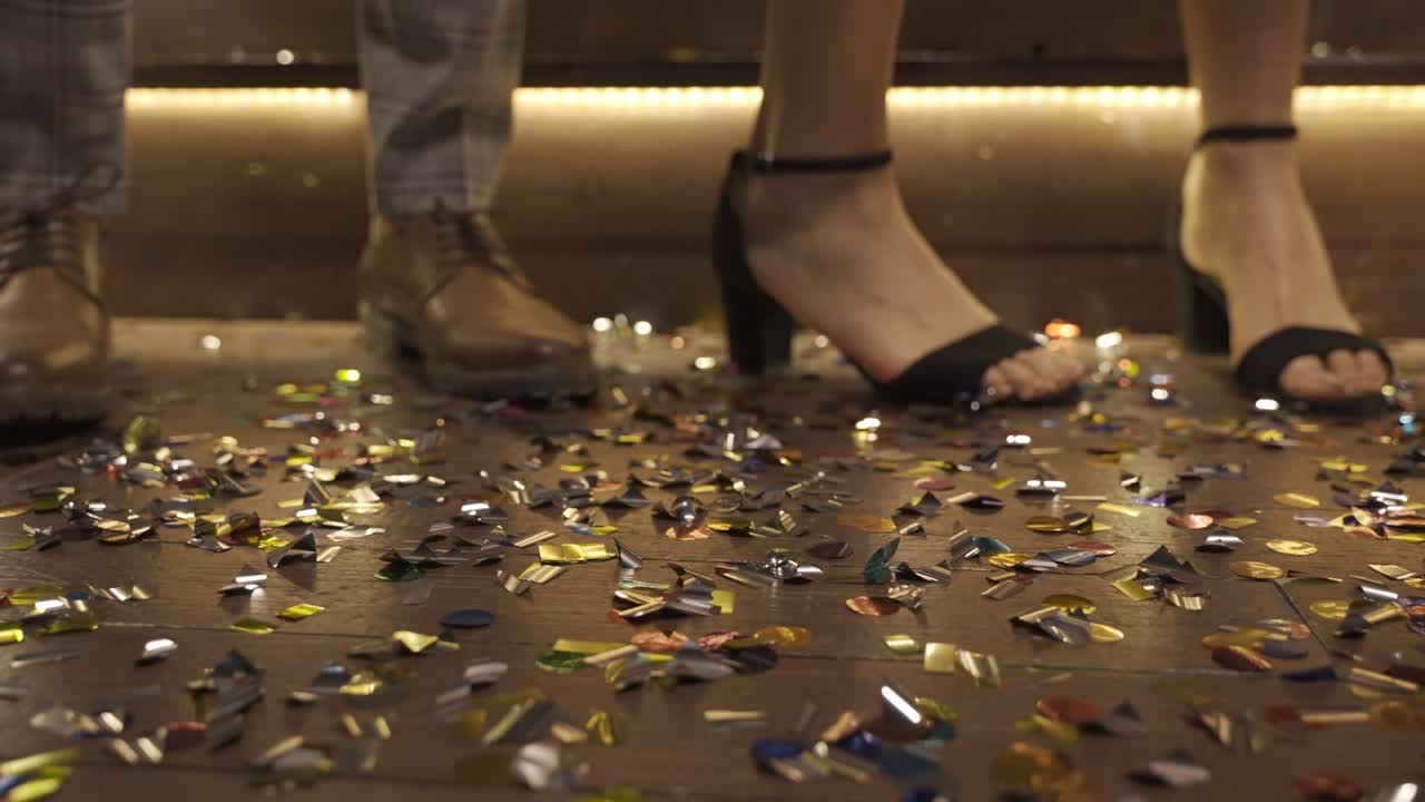 카메라는 춤을 추는 동안 움직이는 색종이와 남자 신발과 여자 발뒤꿈치로 가득 찬 나무 바닥에 초점을 맞춥니다