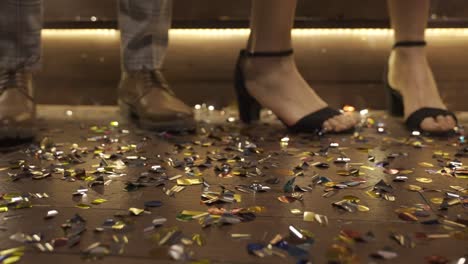 camera focuses on the wooden floor full of confetti and man shoes and woman heels moving while they dance