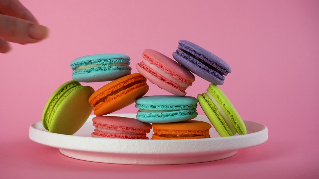 las manos de la mujer toman deliciosos macarrones franceses de colores del plato.