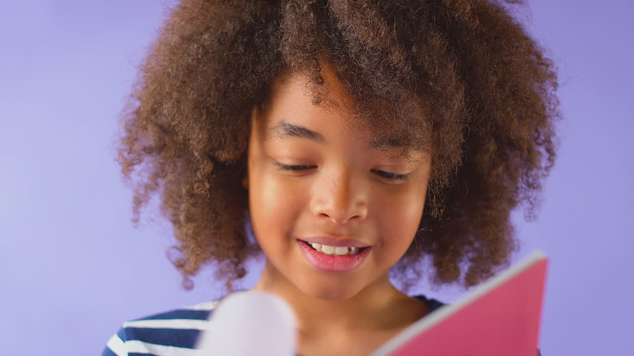 Studio Shot Of Young Boy Studying School Exercise Book Against Purple Background