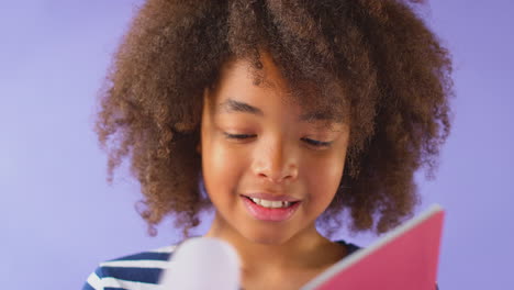 fotografía de estudio de un niño estudiando el libro de ejercicios escolar contra un fondo púrpura