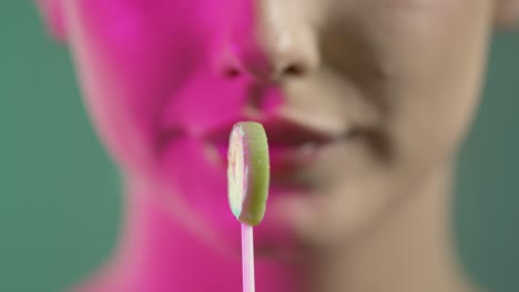 cerca de la cara y la boca de la mujer, chupando lame dulces de piruleta, colorida toma de estudio