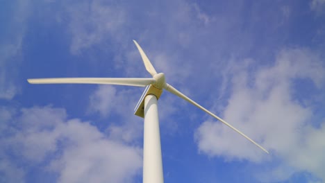 wind turbine turning against bright blue cloudy sky, low angle close view