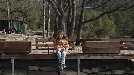 a young female child holds a doll, sits on a ledge and sings, orbital