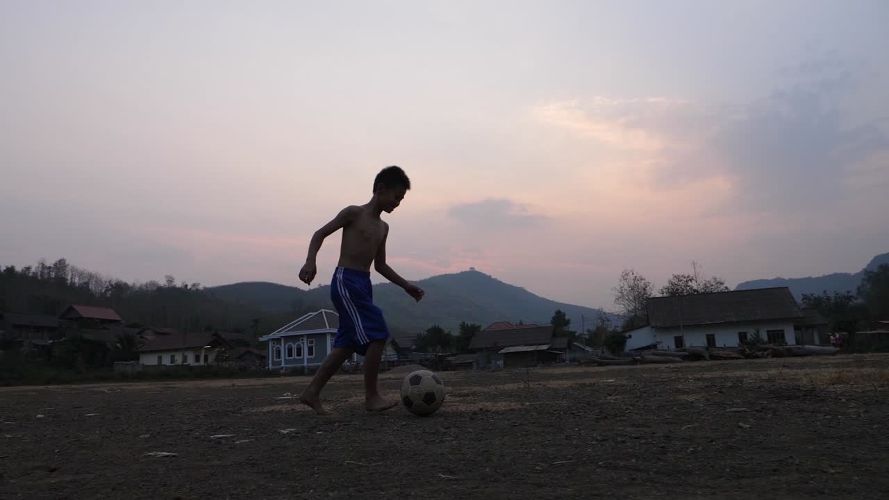 夕暮れの田舎の村でサッカーをする少年