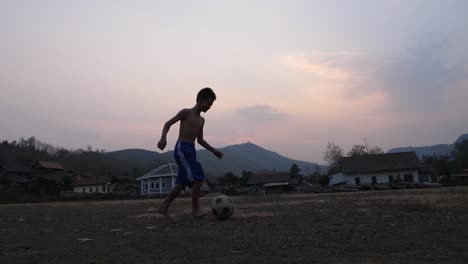 boy playing soccer in a rural village at sunset