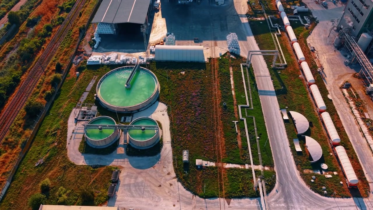 Wastewater treatment facility with circular green pools from above. A top down drone shot captures three round tanks containing bright liquid next to cargo train cars.