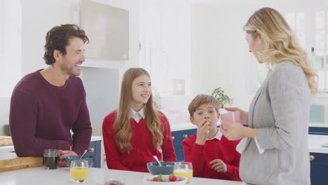 Padres-Ayudando-A-Niños-En-Uniforme-Escolar-A-Prepararse-Mientras-Desayunan-En-El-Mostrador-De-La-Cocina