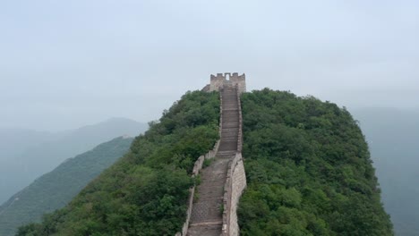 Fly-over-old-rural-part-of-Great-Wall-of-China-with-square-lookout-towers-in-a-distance,-on-cloudy-day