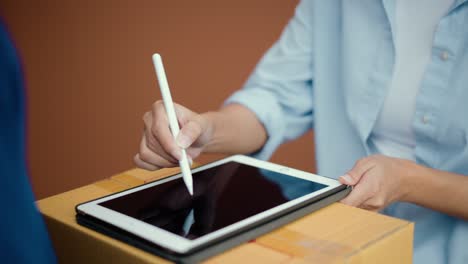mujer de mano firmando firma electrónica en la tableta para el acuerdo del contrato digital recibiendo el paquete del hombre de entrega azul de las compras en línea. mensajero hombre entregando el paquete al destino.