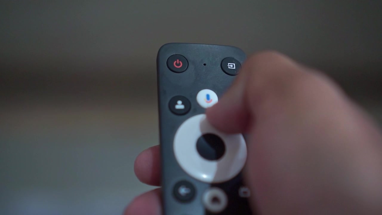 Hånd, der holder en smart-tv-fjernbetjening indendørs. Teknologiske optagelser, der viser streaming, underholdning og dagligdags livsstil i hjemmet