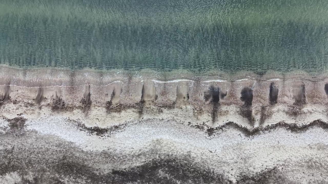 Strandudsigt med sand og vand og en tydelig grænse mellem land og hav i dagtimerne.