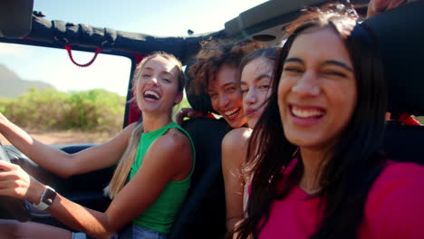 Portrait-Of-Laughing-Female-Friends-Pulling-Faces-In-Open-Top-Car-On-Road-Trip