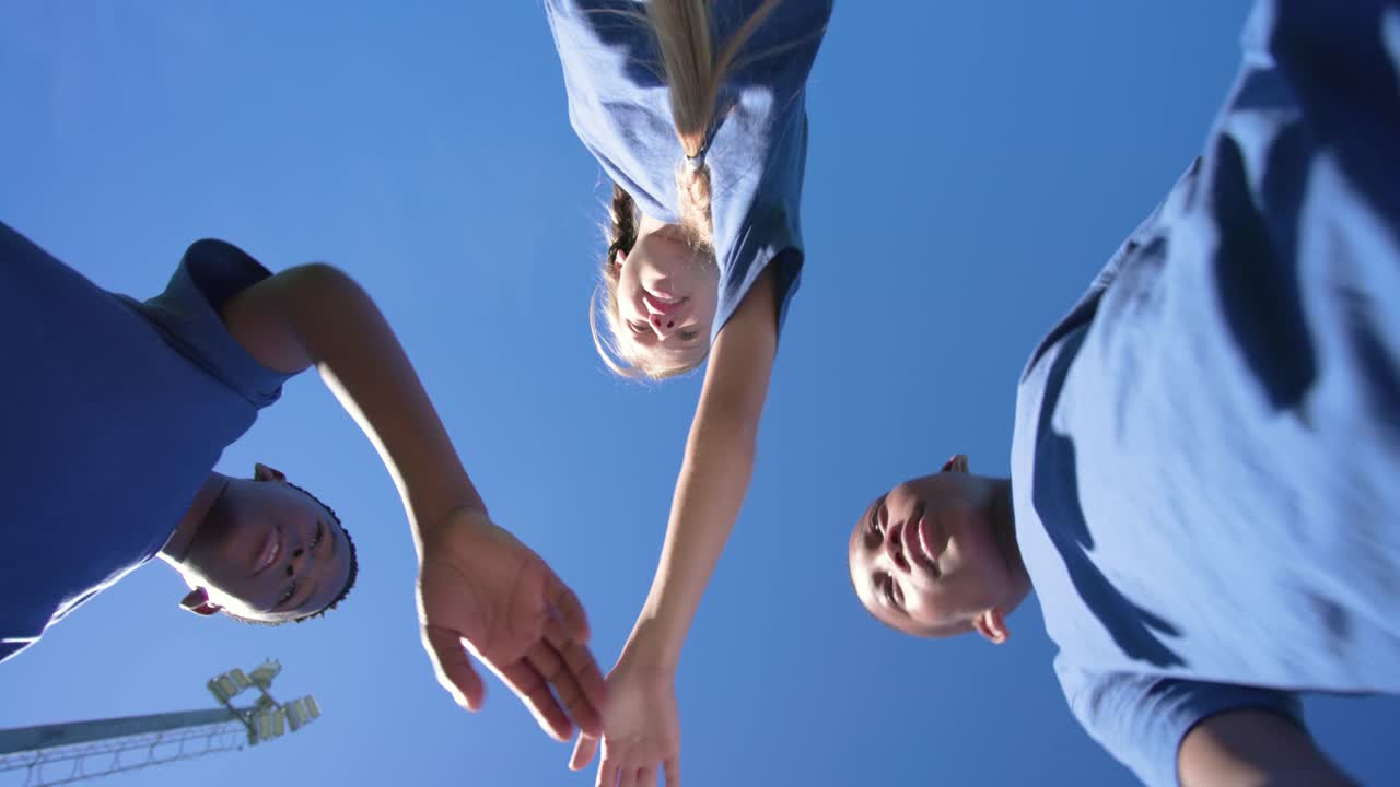Vielfältige Jugendliche in blauen T-Shirts versammeln sich, ein Mädchen mit Zöpfen richtet ihr Shirt und beginnt den Handstapel vor dem Spiel