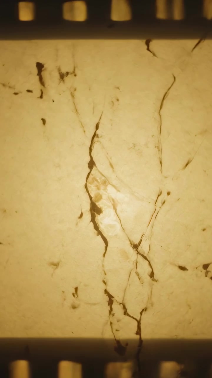 Video verticale: Telecamera che si sposta filmando una pellicola retroilluminata su un tavolo, rivelando una crepa e i fori di trascinamento.