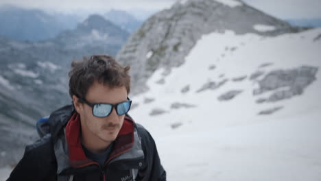 hiker climbing on mountain kanin wearing sunglasses, mountains parially covered in snow in background