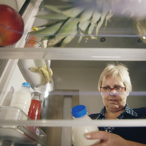 an senior woman takes a bottle of milk from the refrigerator checks the shelf life of the product