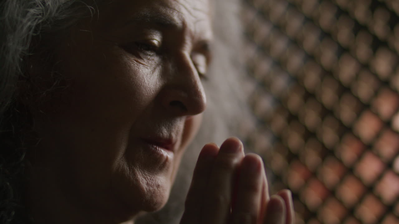 Elderly Woman Praying with Hands Pressed Together in Confessional Booth