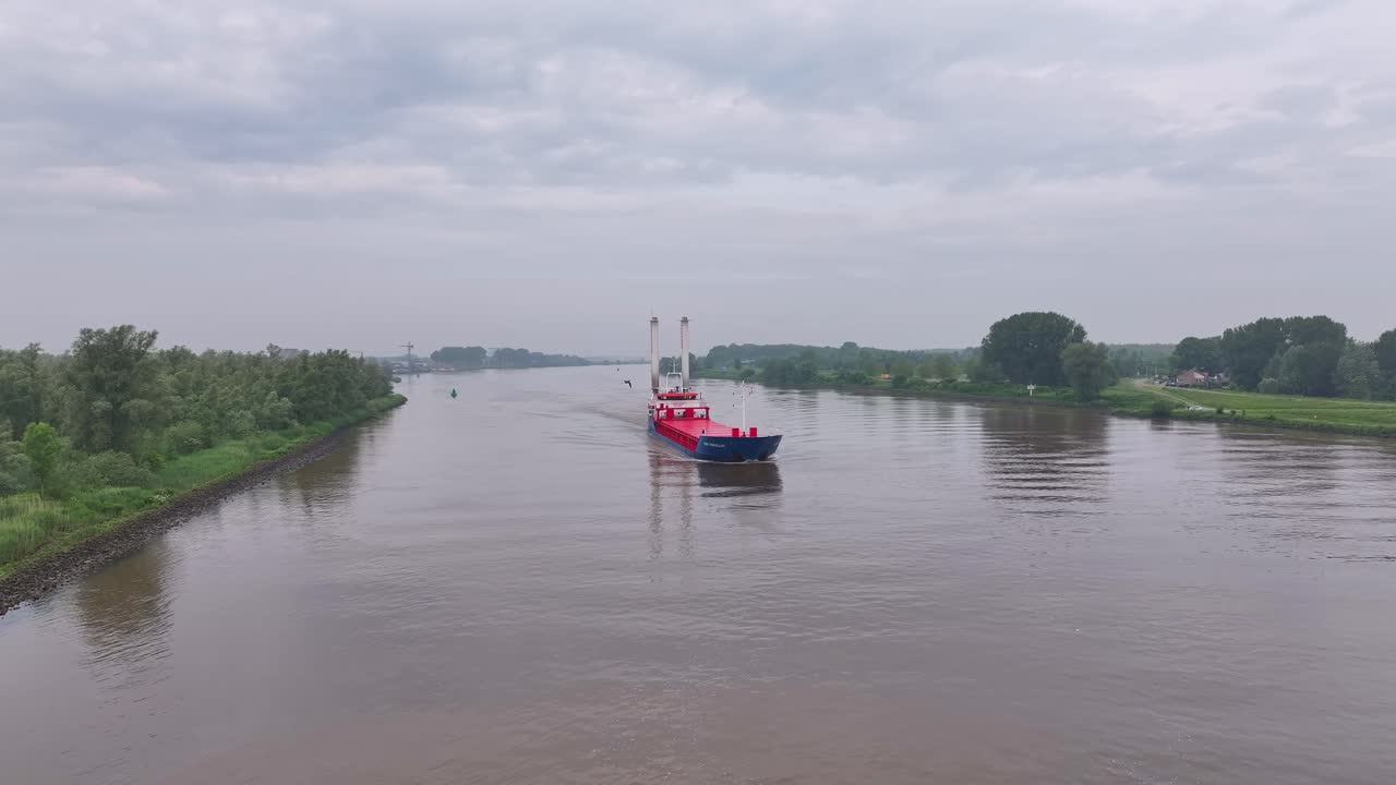 A cargo ship navigates a river or canal under a cloudy sky