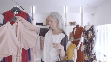 dama de compras enfocada recogiendo el vestido del estante y mirándose en el espejo