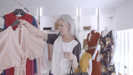 focused shopping lady picking dress from rack and looking at herself on mirror