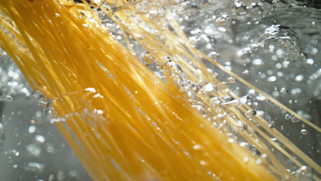 cooking spaghetti: long strands of pasta are dropped into a pot of boiling water - view from below the water's surface, slow motion