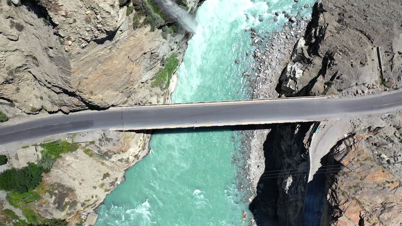 카라코람 고속도로를 따라 카라코람 산맥의 다리 아래로 흐르는 청록색 푸른 물 강의 드론 샷, 공중 촬영 상승