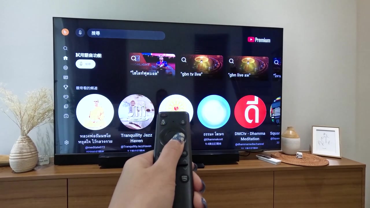 Una mano usa un telecomando per sfogliare varie miniature di video su un grande televisore.