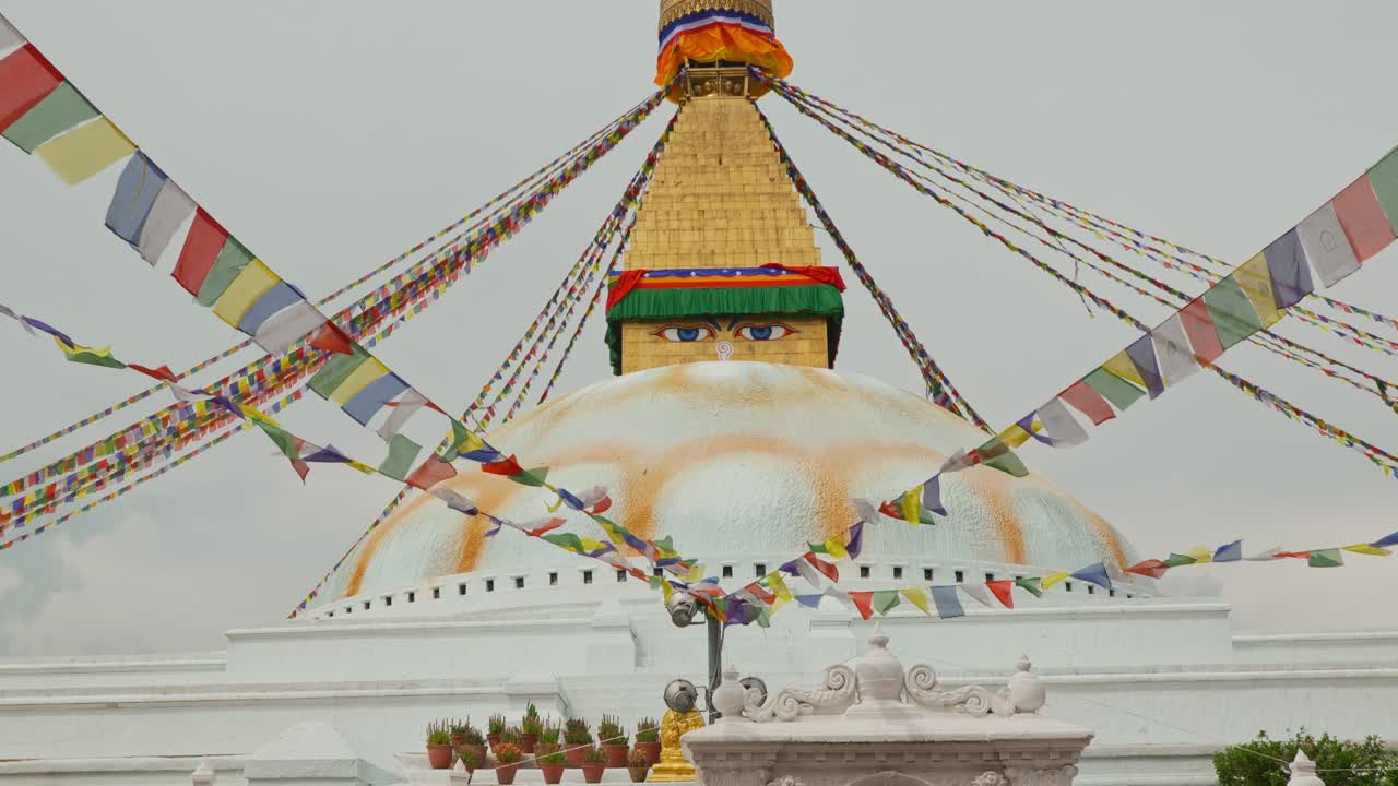Panoramica verso il basso di un elaborato tempio a Kathmandu, Nepal, con dettagli dorati e occhi dipinti, e molti fili di bandiere colorate