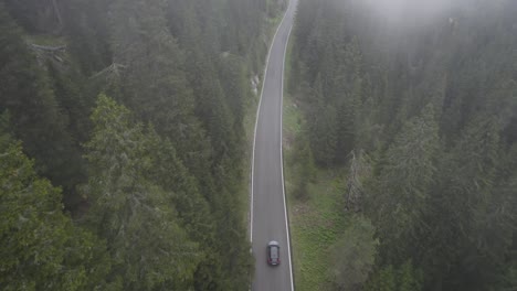 drone shot of a car driving on an empty road in the middle of the forest in passo giao, italy