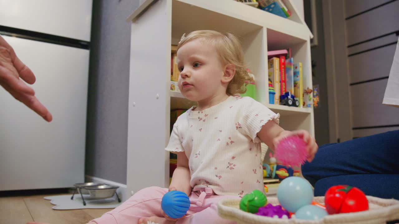 Holčička si hraje s ježatým míčkem a dospělou rukou uvnitř