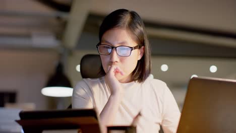 Tired-asian-casual-businesswoman-in-glasses-using-laptop-and-tablet-in-office-at-night,-slow-motion