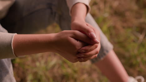 close-up of individual hands clasped together in a calm, reflective pose, resting on knees with soft background of autumn foliage on ground