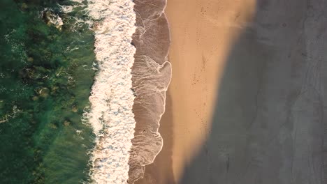 aerial top down view of waves breaking on beach at sunset