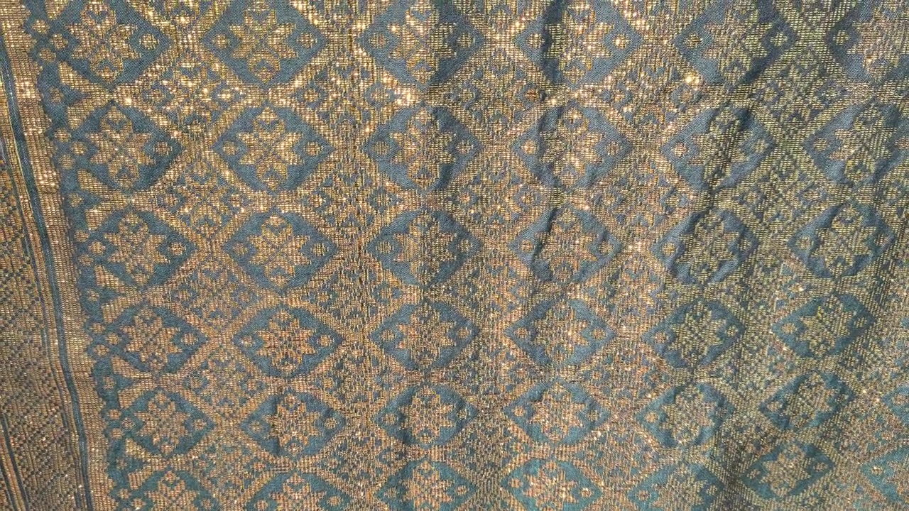 Detailed close-up of luxurious Songket fabric. The intricate gold embroidery shines across the handwoven surface. This prestigious Malaysian textile is reserved for the most special occasions.