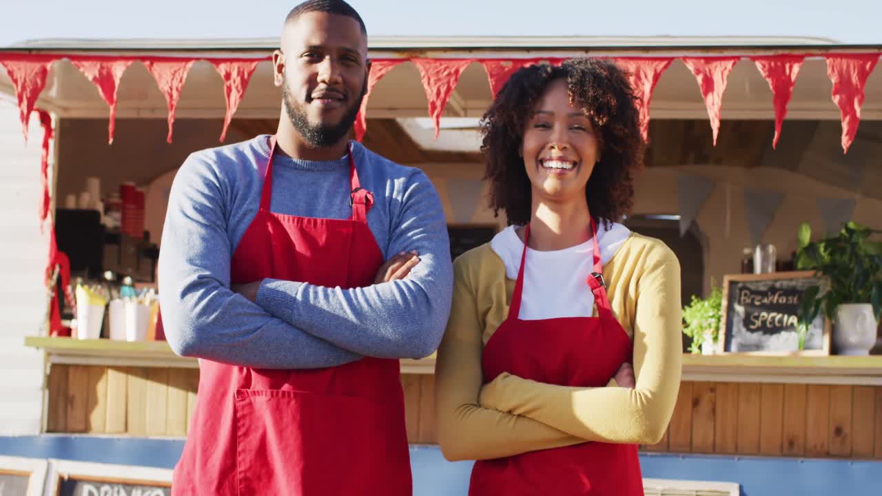 Ritratto di coppia afroamericana a braccia incrociate, sorridente mentre è in piedi vicino al food truck.