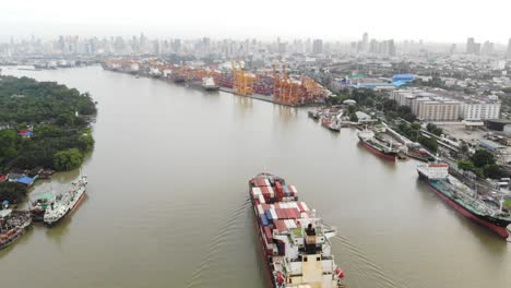 aerial view over container carrier ship cruising along chao phraya river heading to port of bangkok, thailand.