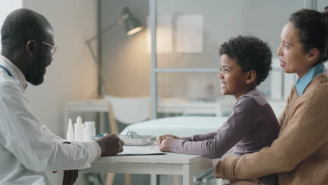 african american boy sitting with mom and talking with doctor in medical office
