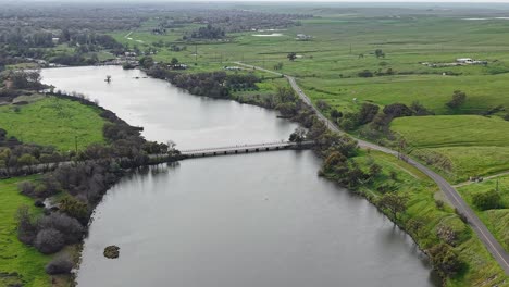 the merced bridge stretches across the flowing river, framed by rolling hills and open skies in this aerial view.