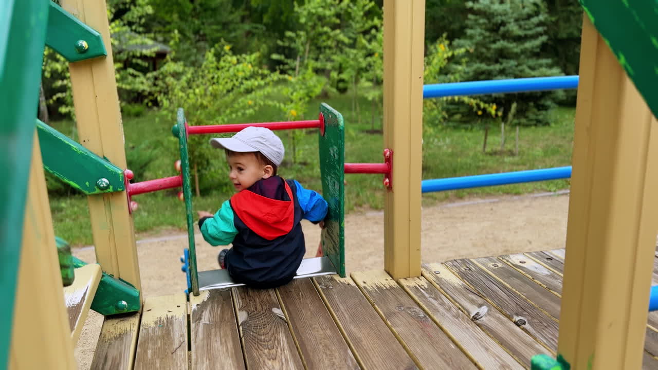 Rear view of a toddler sitting on the slide. Kid turns and smiles to camera and slides down.