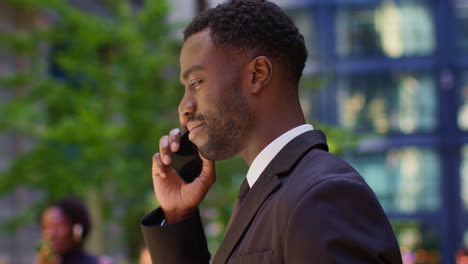 close up of smiling young businessman wearing suit talking on mobile phone standing outside offices in the financial district of the city of london uk 1
