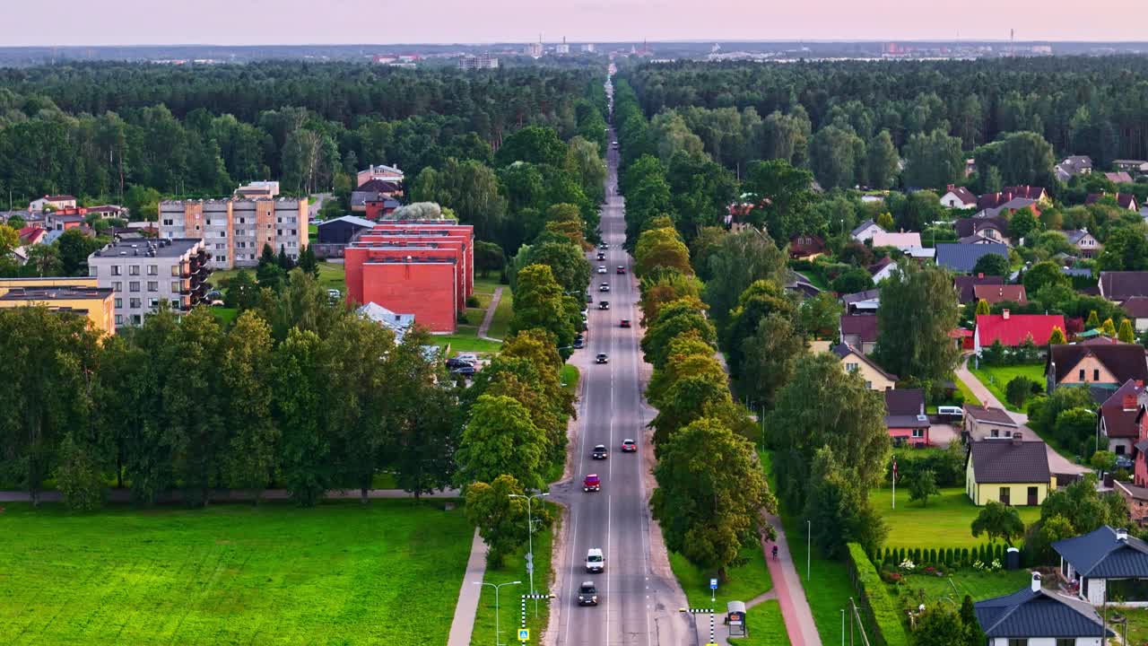 Tree-lined road through Ozolnieki, Latvia with moving cars and residential houses around