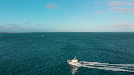 Ferry-boat-on-blue-ocean-with-Stewart-Island-in-the-background-on-beautiful-sunny-day---Bluff,-New-Zealand---Aerial-Drone