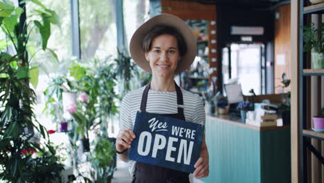woman at a flower shop holding an open sign