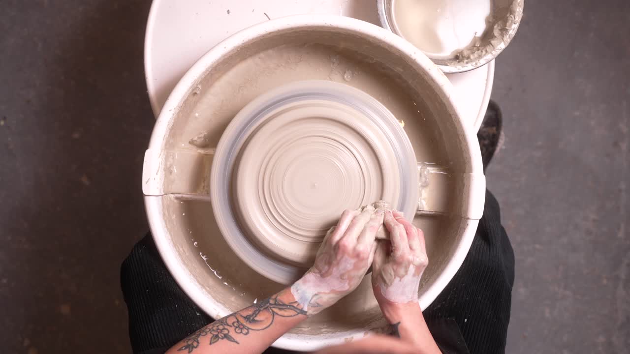Close-up shot of hands doing pottery view from above, pressing thumbs on the clay, plate turning on the wheel