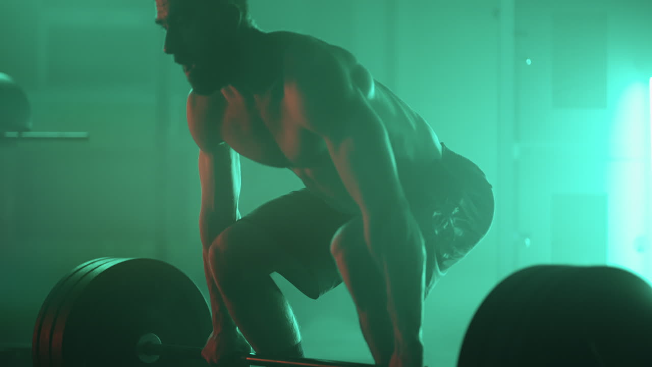 hombre fuerte está haciendo ejercicio solo en el gimnasio en la noche levantando pesas para entrenar la resistencia y los músculos